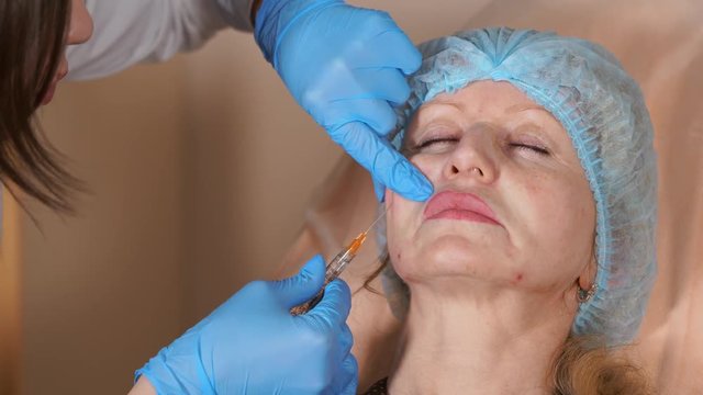 A plastic surgeon in a private clinic injects the cannula into the neck of a middle-aged woman, the drug fillers are in a syringe with a long needle that the doctor moves to the sides.