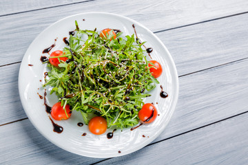 Fresh salad of cherry tomatoes, lettuce, beniseed and sauce on a white plate and white wooden table