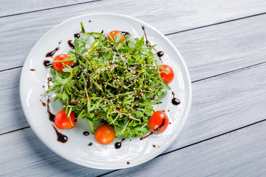 Fresh salad of cherry tomatoes, lettuce, beniseed and sauce on a white plate and white wooden table