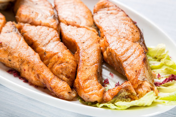 Grilled salmon pieces on white plate with salad. Close up image with selective focus