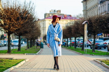 Young beautiful girl in a blue coat and burgundy hat walking down the street on a sunny spring day