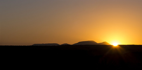 Scenic sunrise over the dessert on the island Fuerteventura Canary Islands with a orange and blue glowing sky and a black skyline of volcanos.