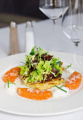 beautifully prepared dish consisting of slices of fresh atlantic Salmon fillet, lightly fried potato cake, mozzarella chunks and salad. All served on a clean white plate.