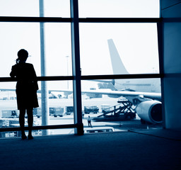 woman standing near the airport window, waiting for flight departure.