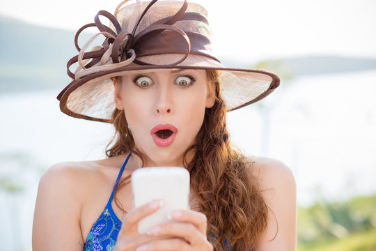 SMS. Closeup portrait funny shocked anxious scared young girl Lady in ha looking at phone seeing bad news photos message with disgusting emotion on face park lake background. Human reaction expression
