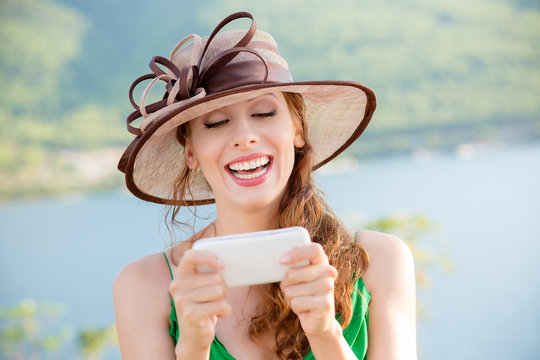 Young Woman in sinamay sun hat  Busy with her Mobile Phone While Walking near the park lake.  Lady in hat at mobile by the sea.