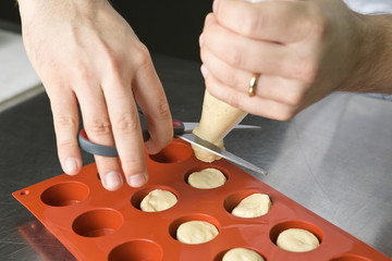 Butter oily pastry dough being squeezed through a basting pipe, into round moulds, ready to be...