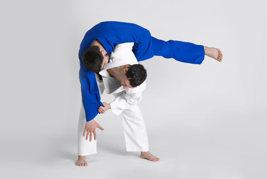 Young sporty men practicing martial arts on light background