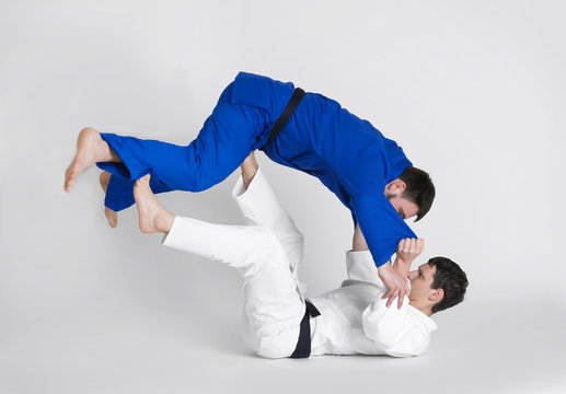 Young sporty men practicing martial arts on light background