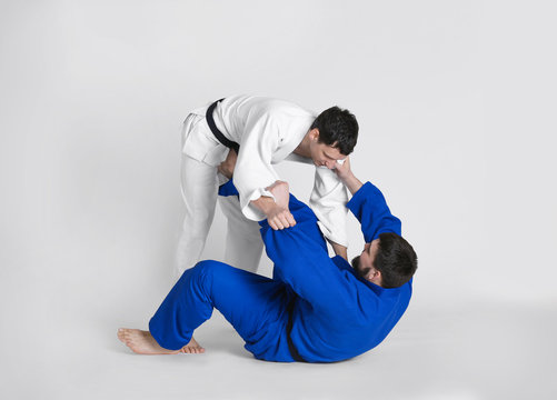 Young sporty men practicing martial arts on light background