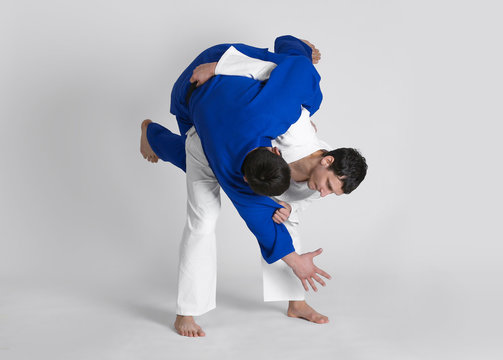 Young sporty men practicing martial arts on light background