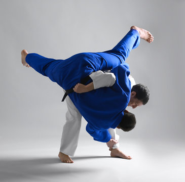 Young sporty men practicing martial arts on light background