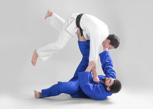 Young sporty men practicing martial arts on light background