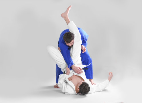 Young sporty men practicing martial arts on light background