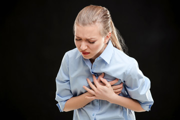 Heart attack concept. Young woman suffering from chest pain on black background