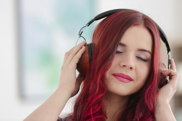 Beautiful young woman with dyed hair listening to music on blurred background