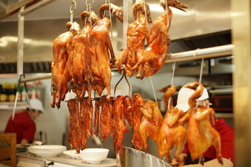 Naklejka premium roasted ducks hung in kitchen with chefs working behind