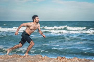 Fototapeta na wymiar Young muscular guy, with a bare torso running along the beach
