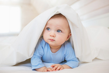 Portrait of thinking little baby hides under a blanket