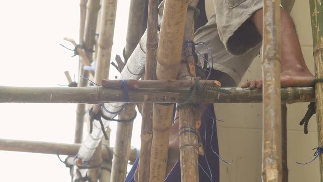 Worker climbing on bamboo scaffold with barefoot