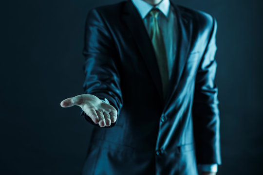 closeup of a businessman stands and extends a hand forward.