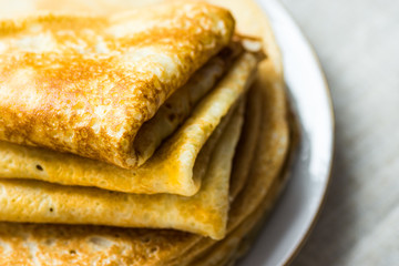 Stacked folded crepes on white plate on linen cloth background, breakfast, cozy morning atmosphere