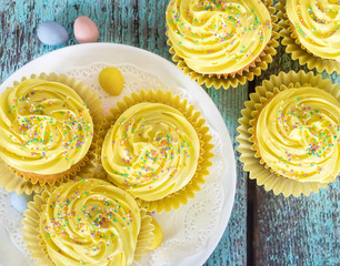Yellow Easter cupcakes with sprinkles and candy eggs on vintage wooden table. Top view.