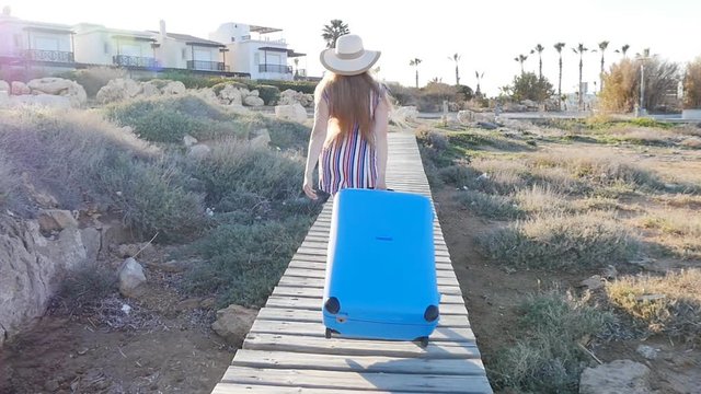 Happy young woman on vacation in a hat with a suitcase