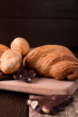 Croissants on board on wooden background. Rustic style. Piece of chocolate.