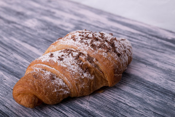 Croissants with powdered sugar and chocolate on colored wood background. Close up
