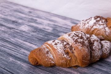 Croissants with powdered sugar and chocolate on colored wood background. Copy space