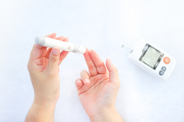 Asian woman hands using lancet on finger to check blood sugar test level by Glucose meter,...