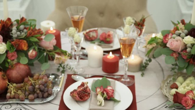 Sharpness of camera focus changing table with bouquets of flowers laying. white tablecloth, fruit for banquet. Two plates opposite each other on red napkins, serviette on dishes, bouquets with pink