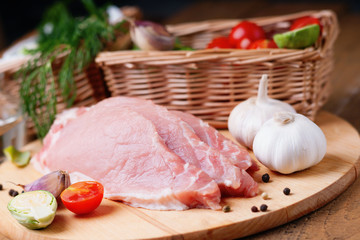 Slices of raw pork meat and wicker basket with vegetables 