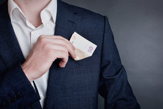 Man in a suit placing money in his jacket pocket.