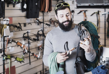 cheerful male customer examining climbing equipment in sports equipment store