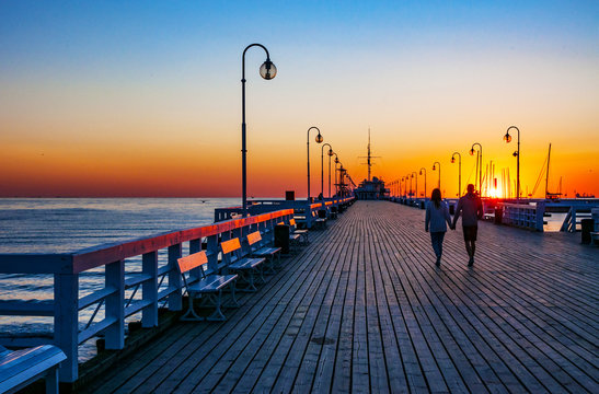 Fototapeta Sunrise at the wooden pier (molo) in Sopot, Poland and an unrecognizable walking couple