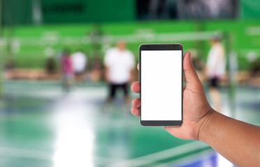 hand hold mobile phone over blurred of badminton court with players playing badminton.