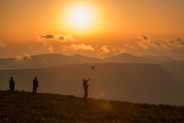 photographers at sunrise high in the mountains launching quadcopter, soft warm background
