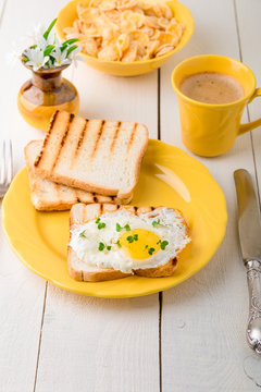 Toast with egg in yellow plate near vase with flower on white wooden background. Healthy breakfast
