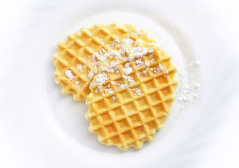 Two beautiful appetizing golden crispy waffles  lie on a white plate sprinkled with powdered sugar close-up view from above.