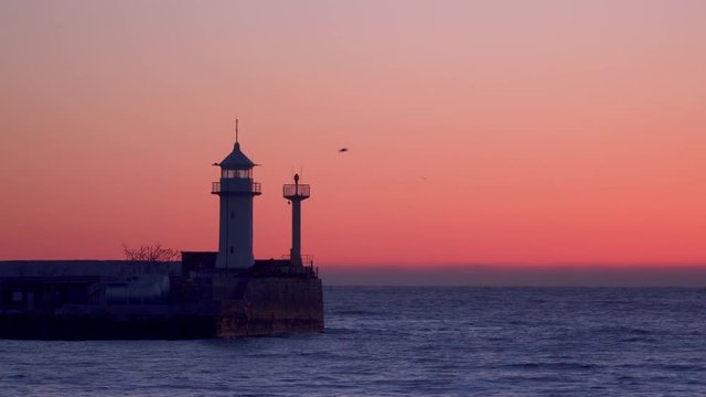 A pier with a flashing lighthouse at dawn. Yalta Crimea.