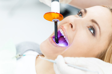 Close-up partial view of dentist using dental curing UV lamp on teeth of patient