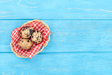 Three fresh quail eggs in a basket on an empty wooden background, top view