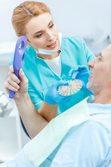 Professional dentist with samples comparing teeth of mature patient looking at mirror