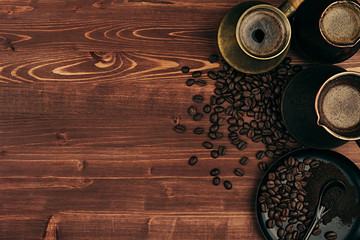 Fototapeta premium Hot coffee in shabby turkish pots cezve with beans, saucer with copy space on brown old wooden board background, top view. Rustic style.