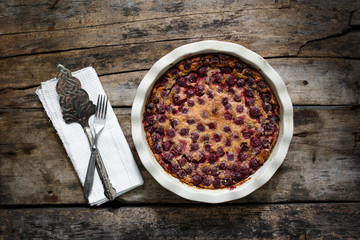 Top view of Cherry clafoutis with spatula on wooden background
