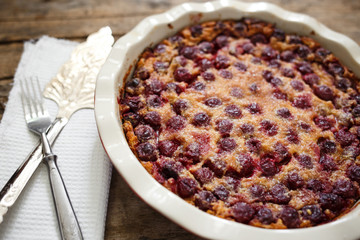 Cherry clafoutis pie in ceramic baking dish with spatula on wooden board