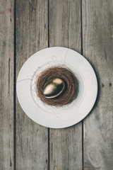 Top view of golden Easter egg in nest on white plate on wooden table, Happy Easter concept