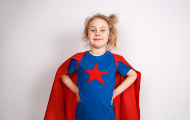 Six year blonde girl dressed like superhero having fun at home. White wall on background